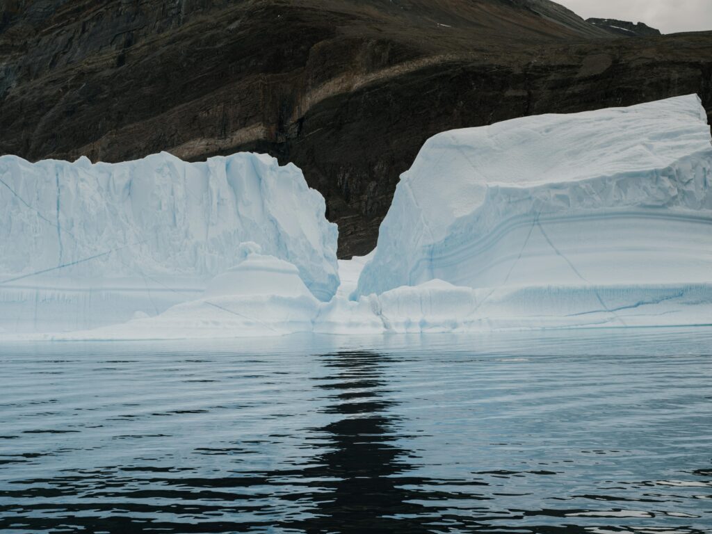 A stunning iceberg floating in serene Arctic waters against a rocky mountain backdrop.